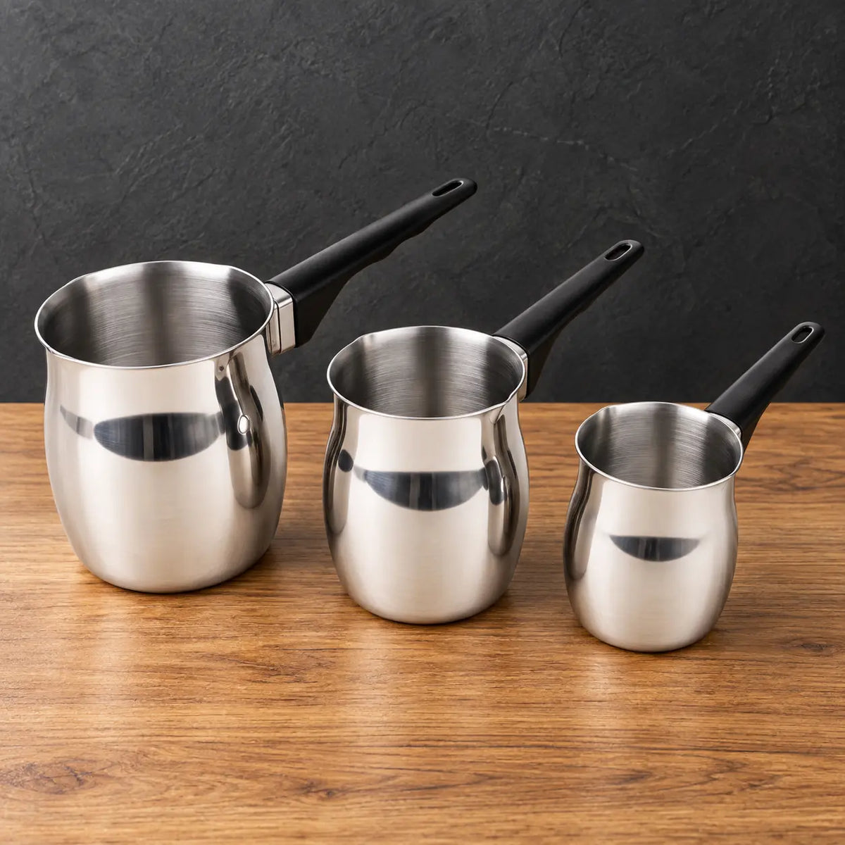 Three polished stainless steel milk cups with black handles