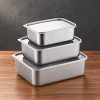 Three deep rectangular stainless steel food storage containers stacked with light-colored lids