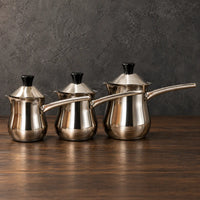 Three lidded stainless steel milk cups with extended metal handles