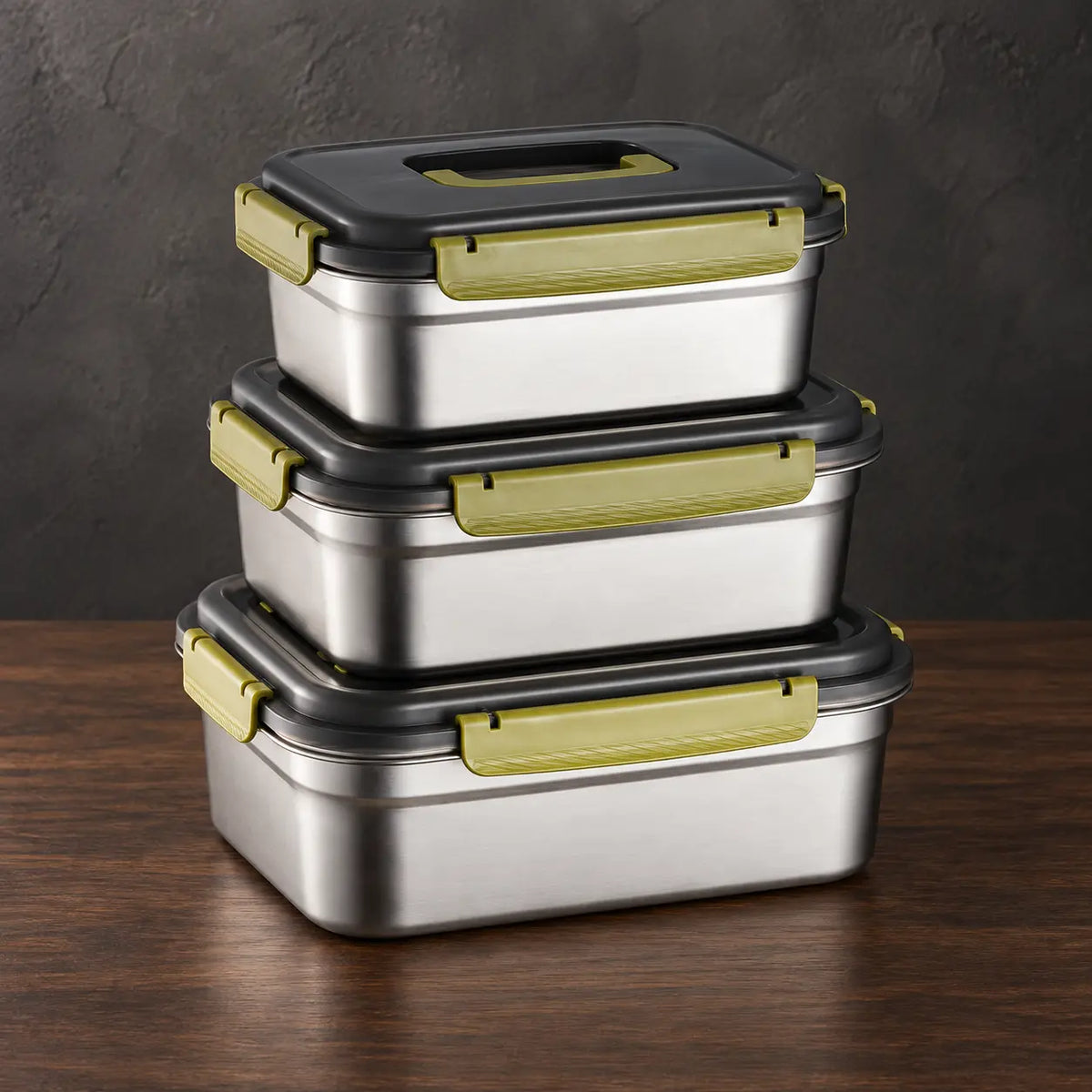 Three rectangular stainless steel food storage containers stacked with black lids and olive-toned side latches