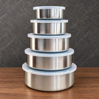 Nested round stainless steel food storage containers with translucent lids beside product packaging