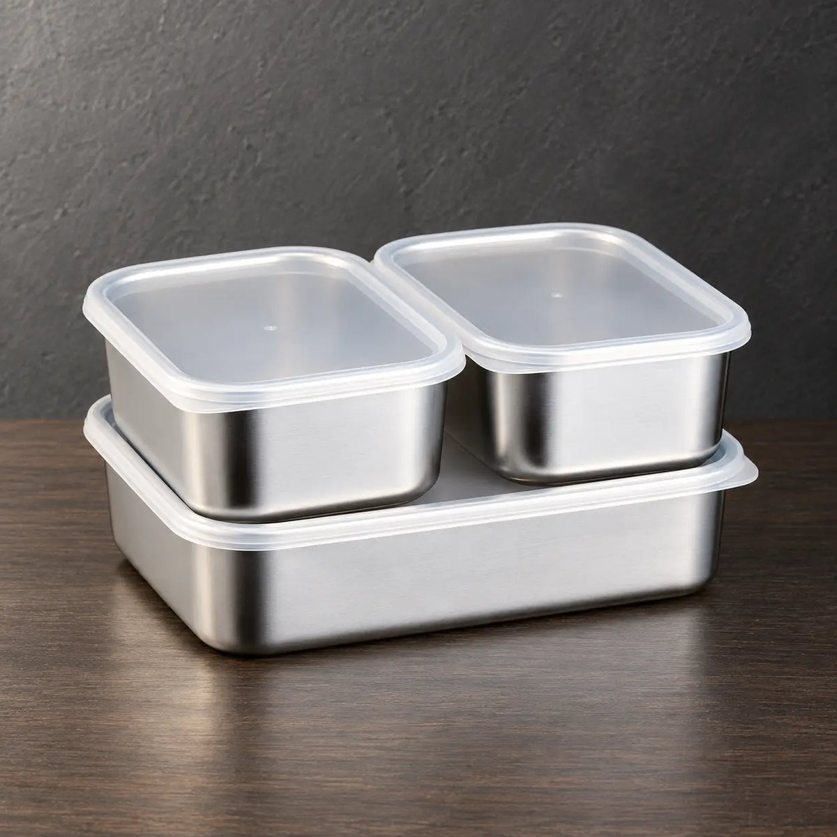 Three rectangular stainless steel food storage containers stacked from smallest to largest with light-colored lids